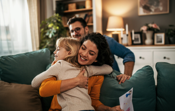 Mother hugging young girl with father in the background - Foster Care Mother hugging young girl with father in the background - Foster Care