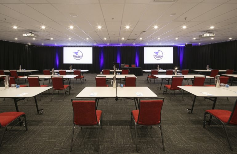 Distant front view shot of the Smith Room at the Wesley Conference Centre, with Wesley Mission logos showing on two digital screens
