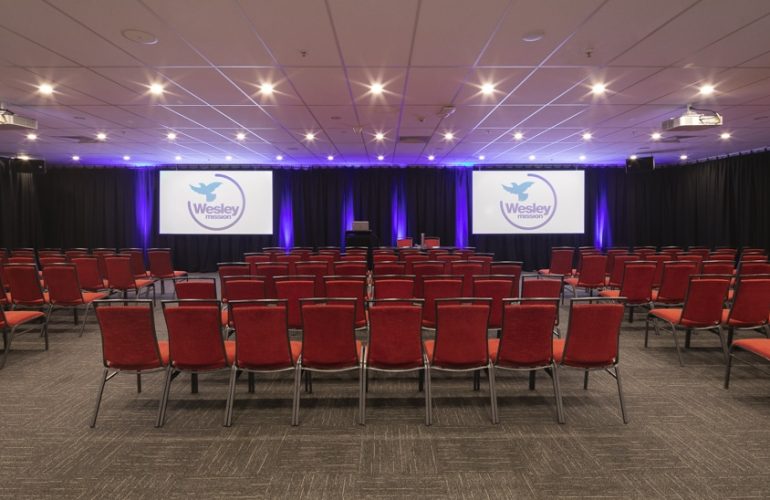 Medium front view shot of the Smith Room at the Wesley Conference Centre, with Wesley Mission logos showing on two digital screens