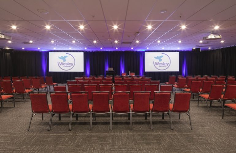 Medium front view shot of the Smith Room at the Wesley Conference Centre, with Wesley Mission logos showing on two digital screens
