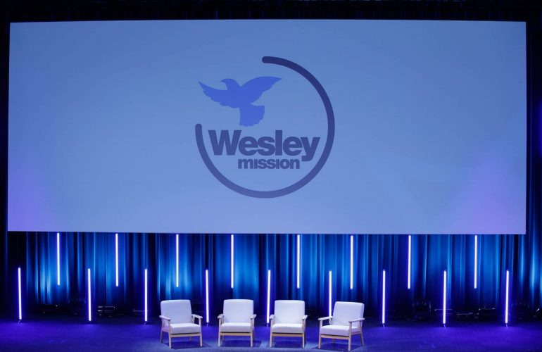 Medium front view shot of the Wesley Theatre with Wesley Mission logo showing on digital screen above the stage,